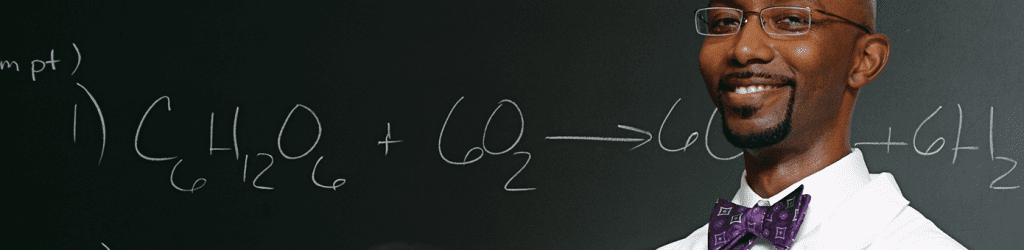 Professor in front of chemical formula on blackboard