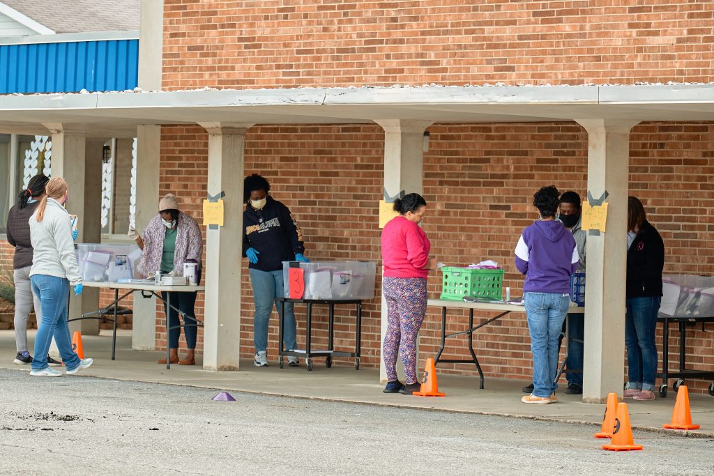 Parents line up outside Moss Street Partnership school; faculty and staff stand behind tables distributing tablets
